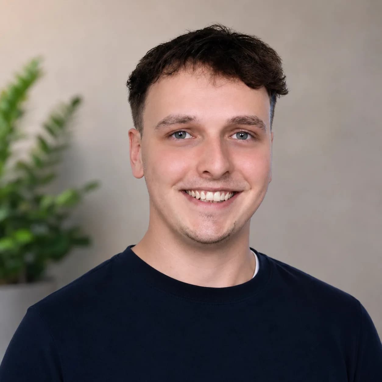 Porträt von Konrad Mayer vor einer hellen Wand mit Pflanze